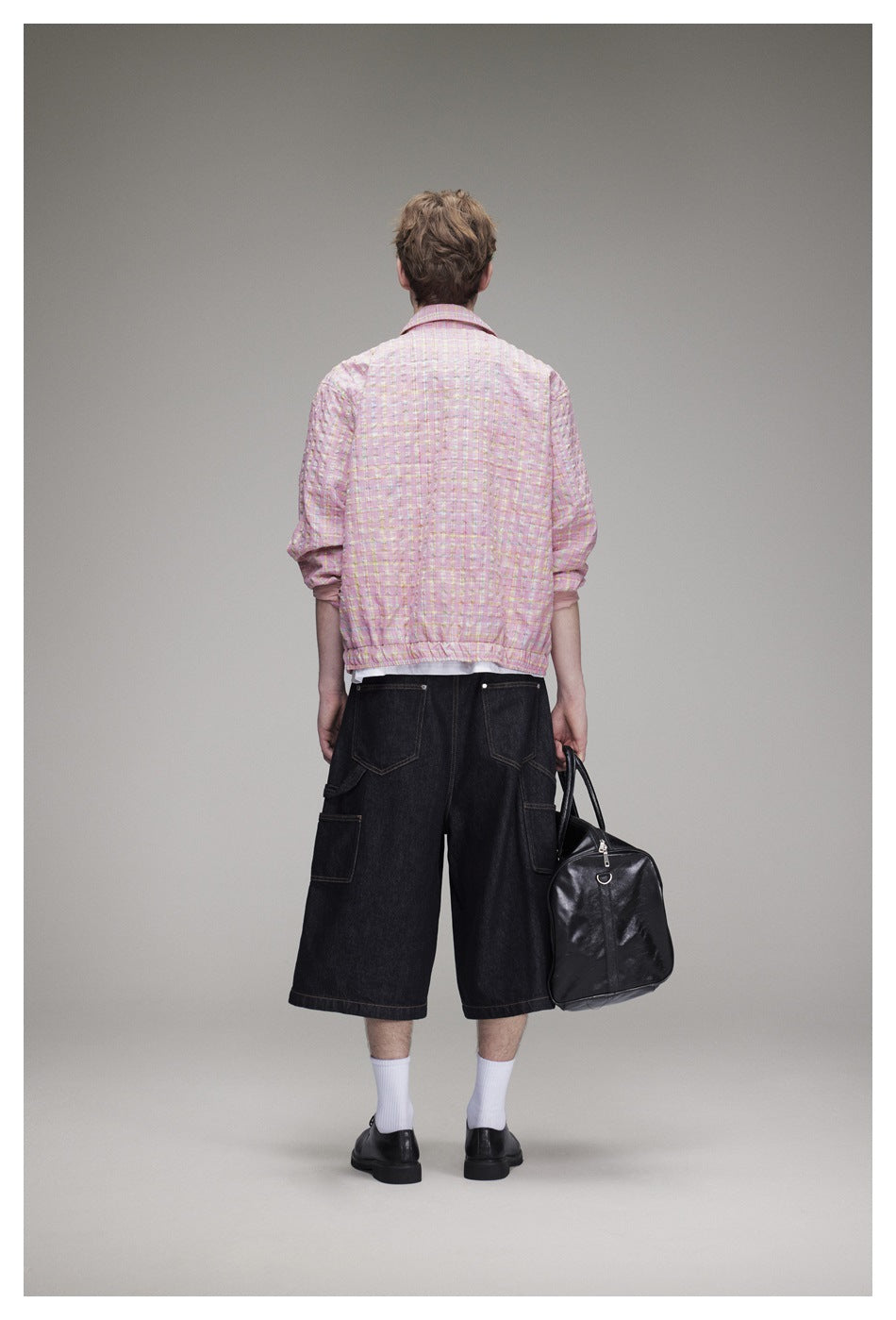 Back view of model wearing the pink checked jacket with elasticated hem, dark denim shorts and a black bag