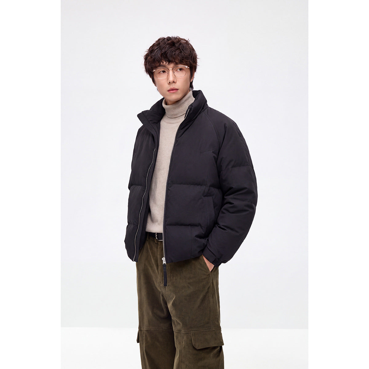 Model wearing a black padded zip-front jacket with a high collar over a light beige turtleneck.