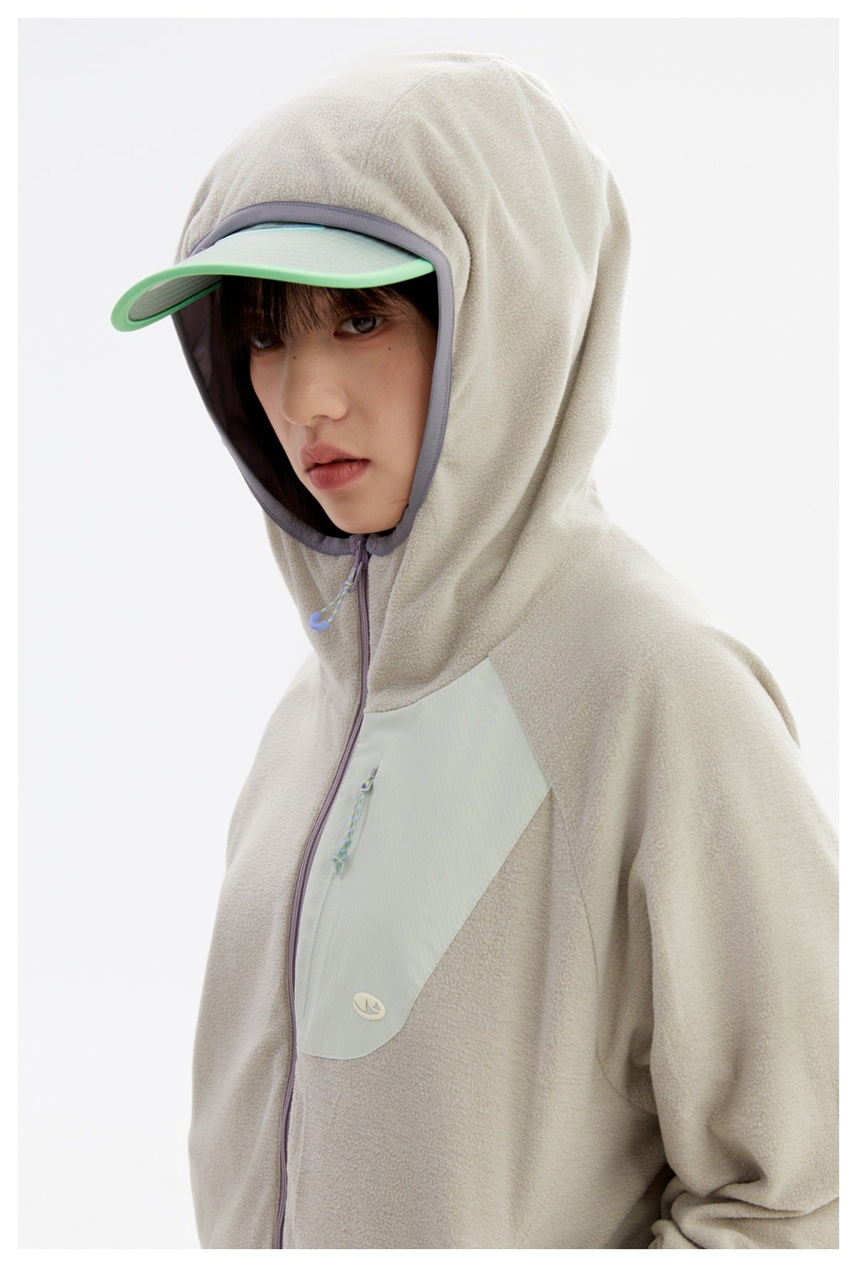 Close-up of a model wearing a light beige hooded jacket with a pale mint chest panel and green-edged visor.