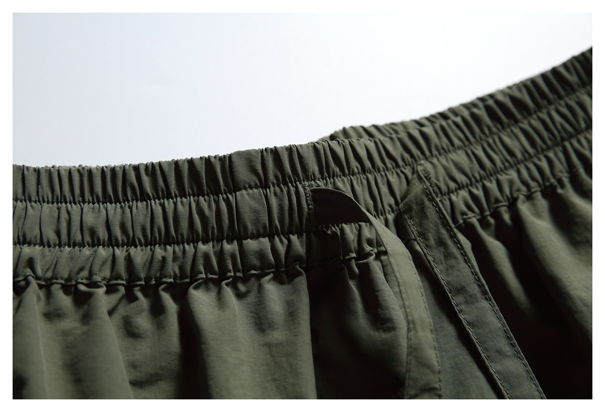 Close-up of dark olive shorts with a gathered elastic waistband and narrow hanging drawstrings.