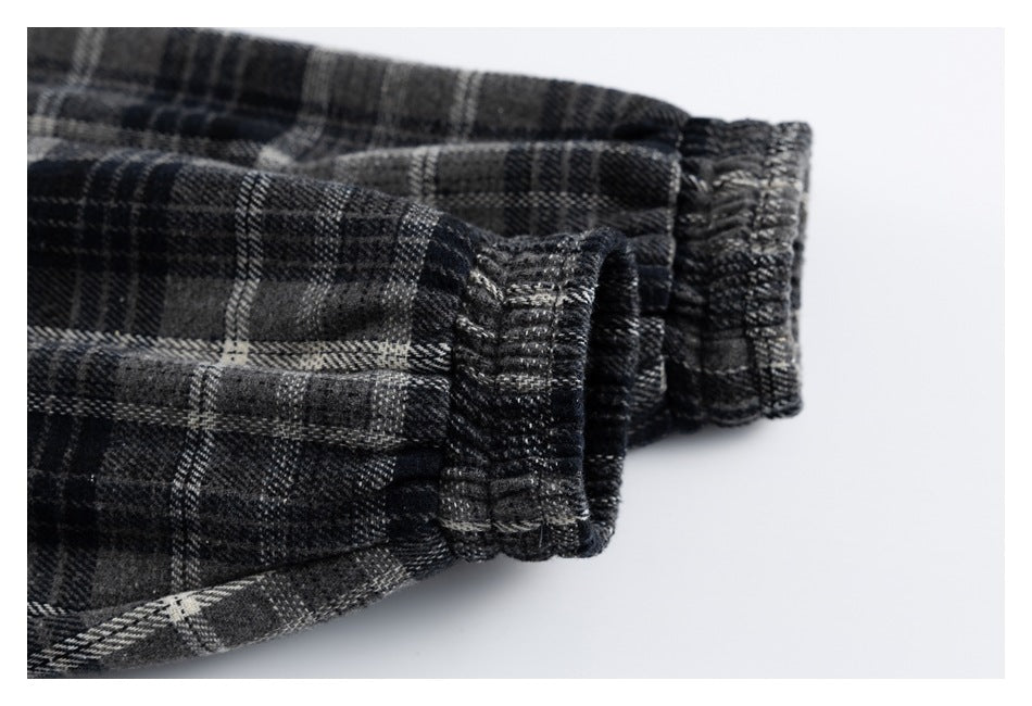 Close-up of a gathered cuff on a black and gray plaid garment against a white background.