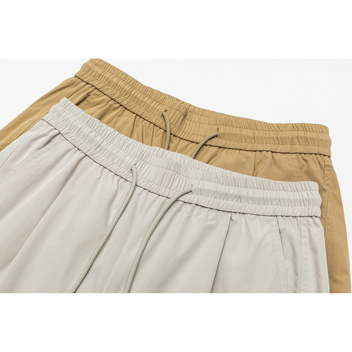 Close-up of tan and light gray pants showing elastic drawstring waistbands and front seams.