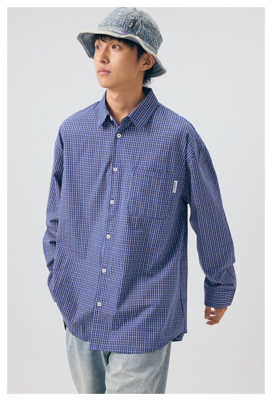 Model wearing a blue check button-up shirt with chest pocket, a denim bucket hat and light jeans