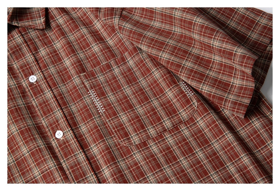 Close-up of a rust-red plaid button-up shirt showing a white button and chest pocket with decorative stitching.