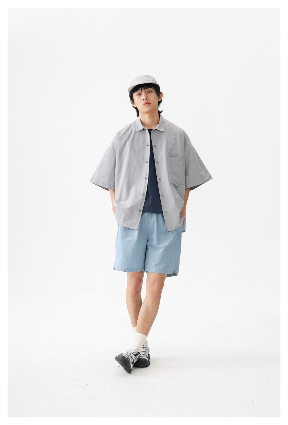 Front view of a model wearing an oversized light gray short-sleeve button-up shirt and pale blue shorts.