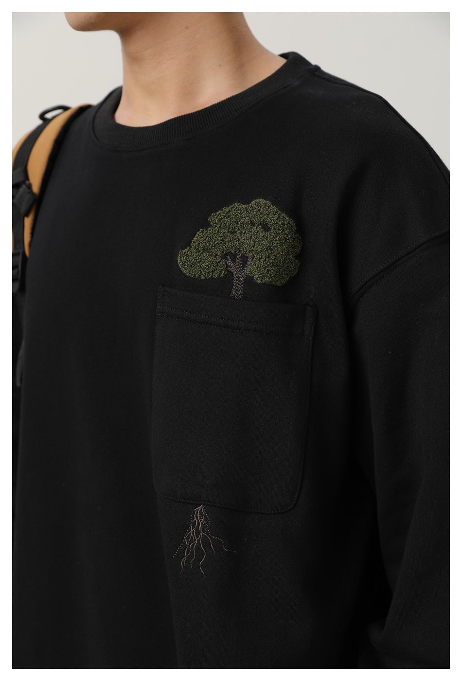 Close-up of a black sweatshirt's chest pocket with an embroidered tree and roots motif.