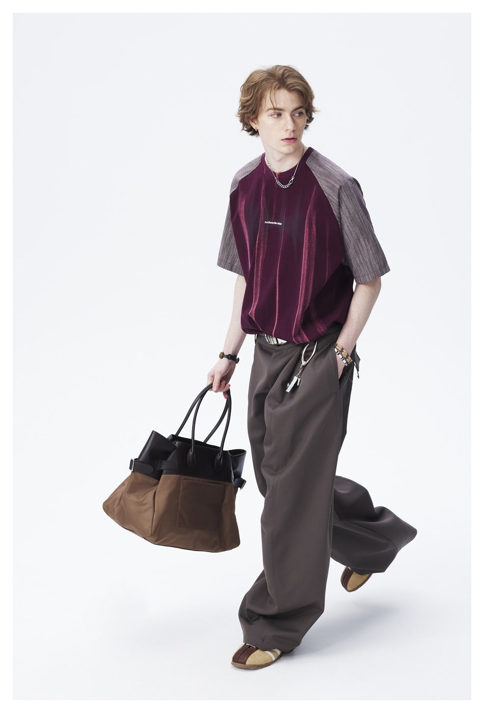 Model wearing a burgundy shirt with gray striped raglan sleeves and wide charcoal trousers, carrying a large two-tone tote.