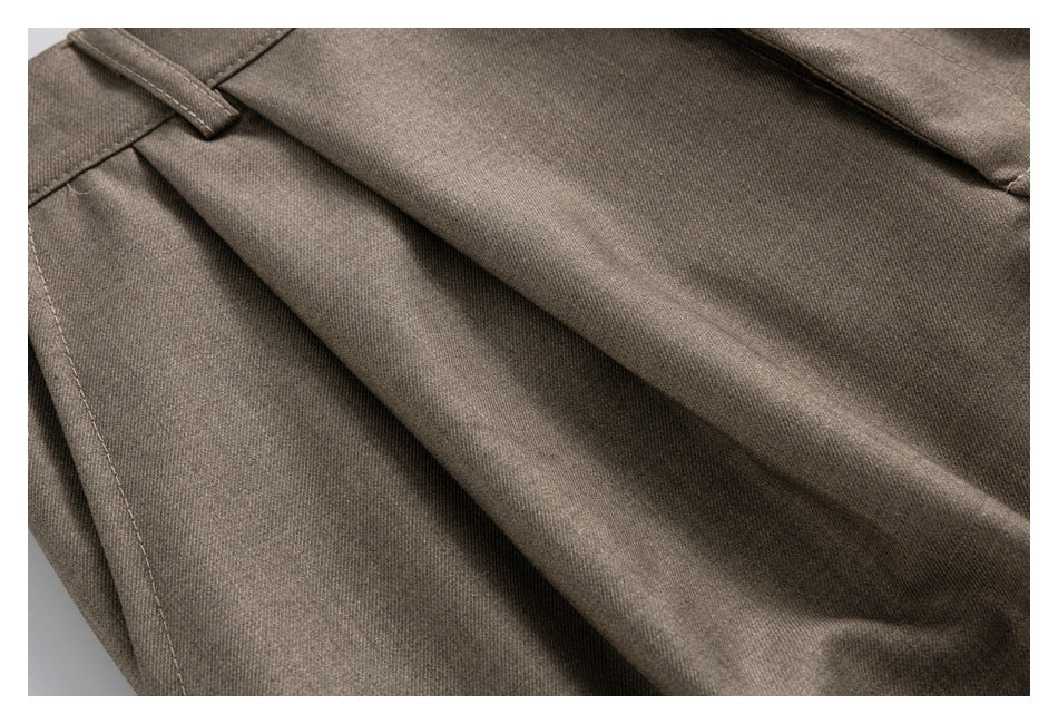 Close-up of taupe-brown trouser fabric, front pleats and stitching.