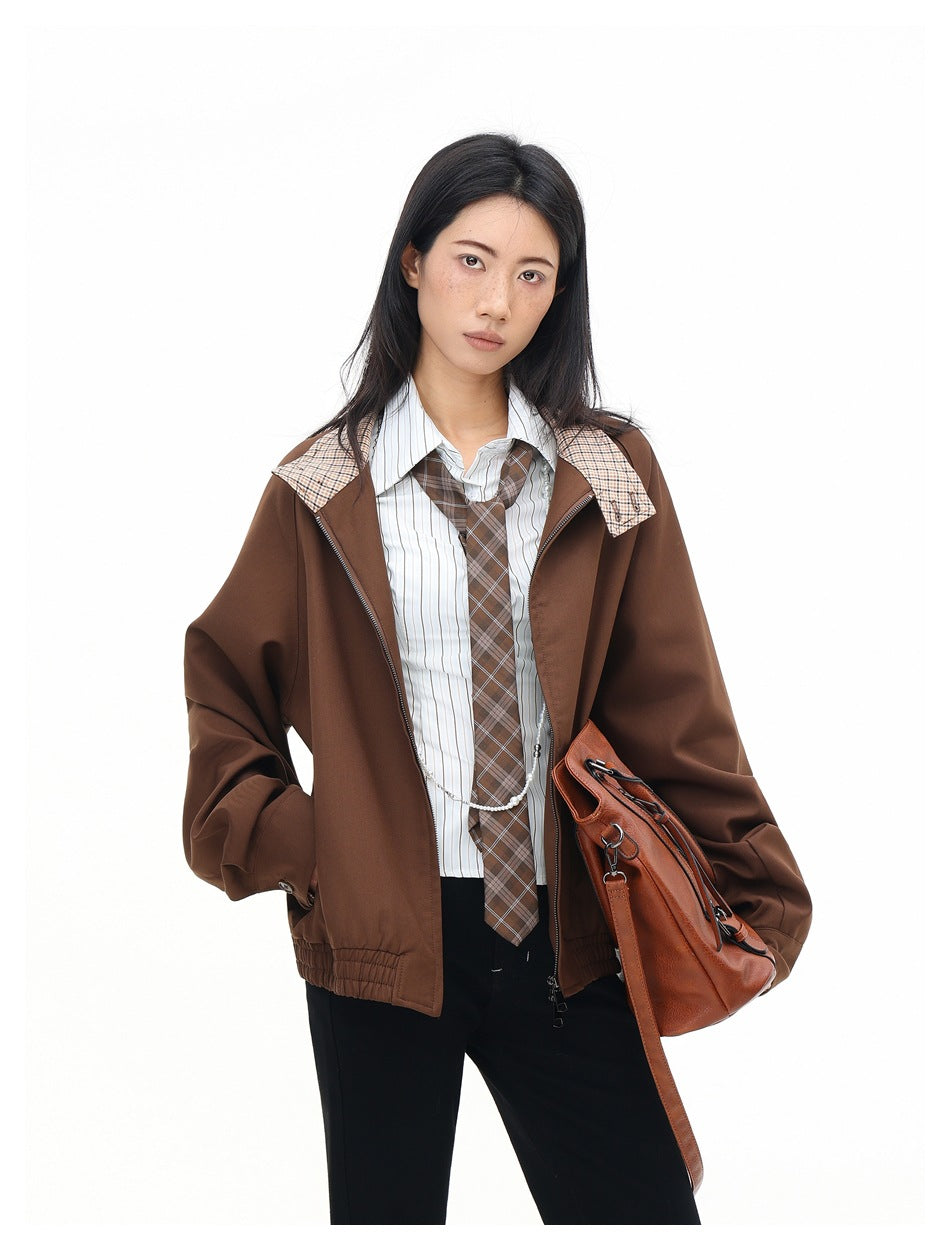 Model wearing an open brown jacket with plaid collar accents over a striped shirt and plaid tie, carrying a brown bag.