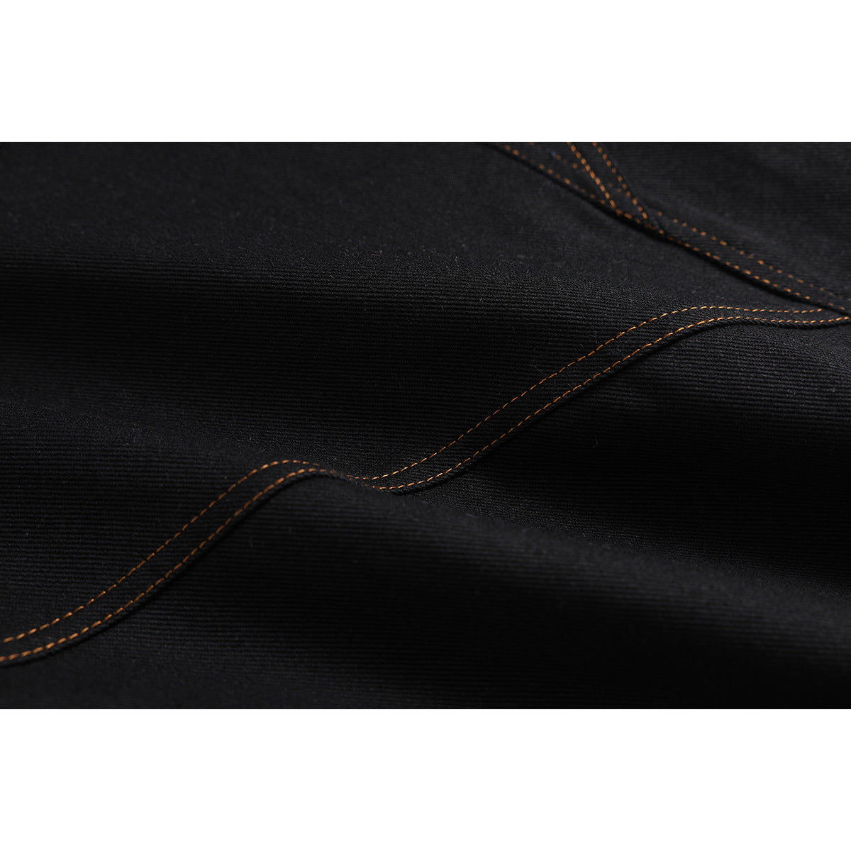 Close-up of black denim with a curved seam traced by orange stitching.