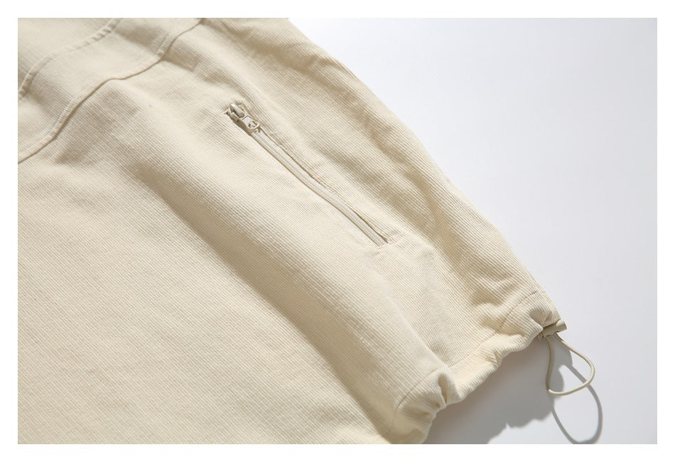 Close-up of a cream ribbed garment showing a vertical zip pocket and drawcord hem.