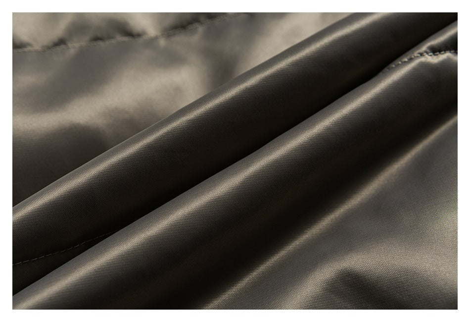 Close-up of smooth, glossy charcoal-olive garment fabric folded into soft ridges with a stitched seam.