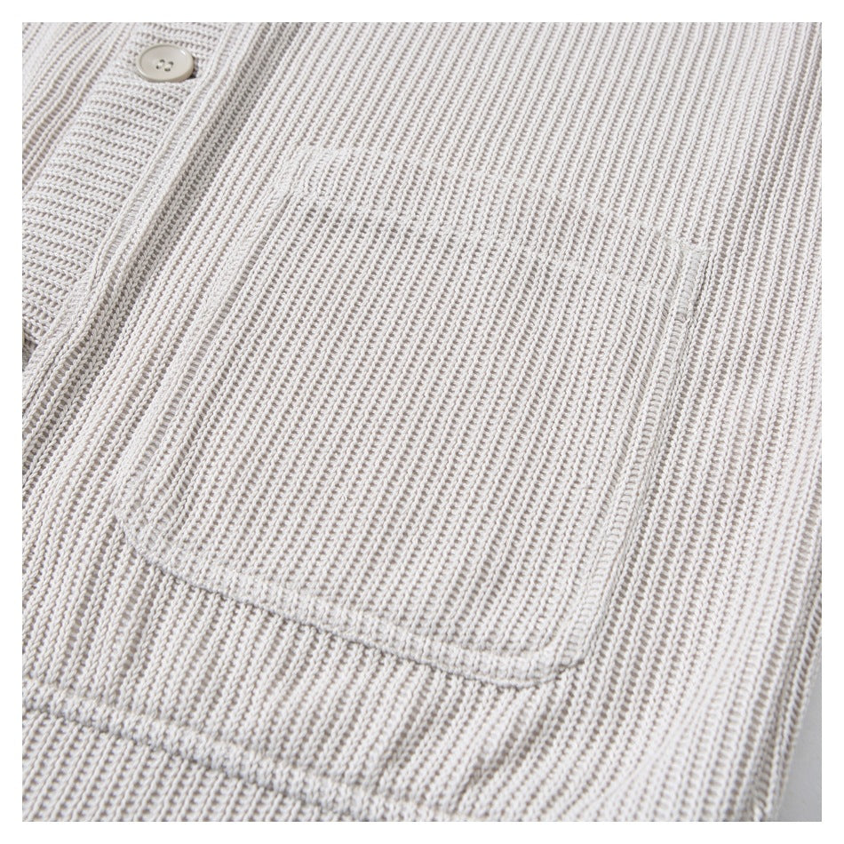 Close-up of a large patch pocket and button placket on a light beige rib-knit cardigan.