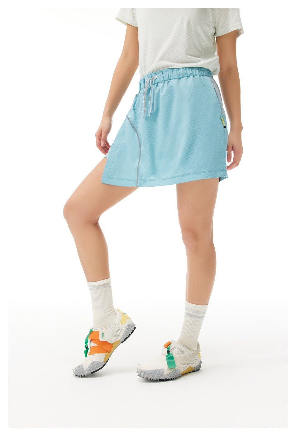 Angled side view of a model wearing a light blue athletic skirt with an elastic drawstring waist.