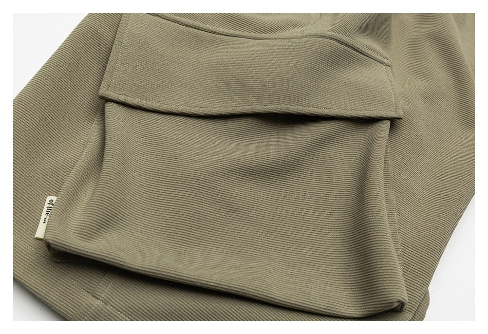 Close-up of olive-khaki ribbed garment fabric folded to show a wide stitched edge and small sewn label.