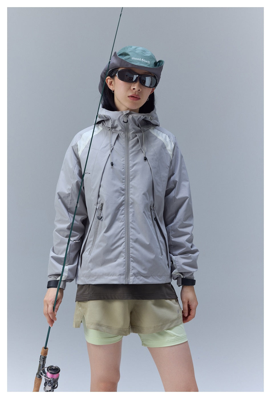 Woman wearing a zipped light gray hooded jacket with beige shorts, shown from the front.