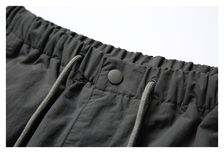 Close-up of charcoal pants with an elastic waistband, drawcords, and a snap-button tab.