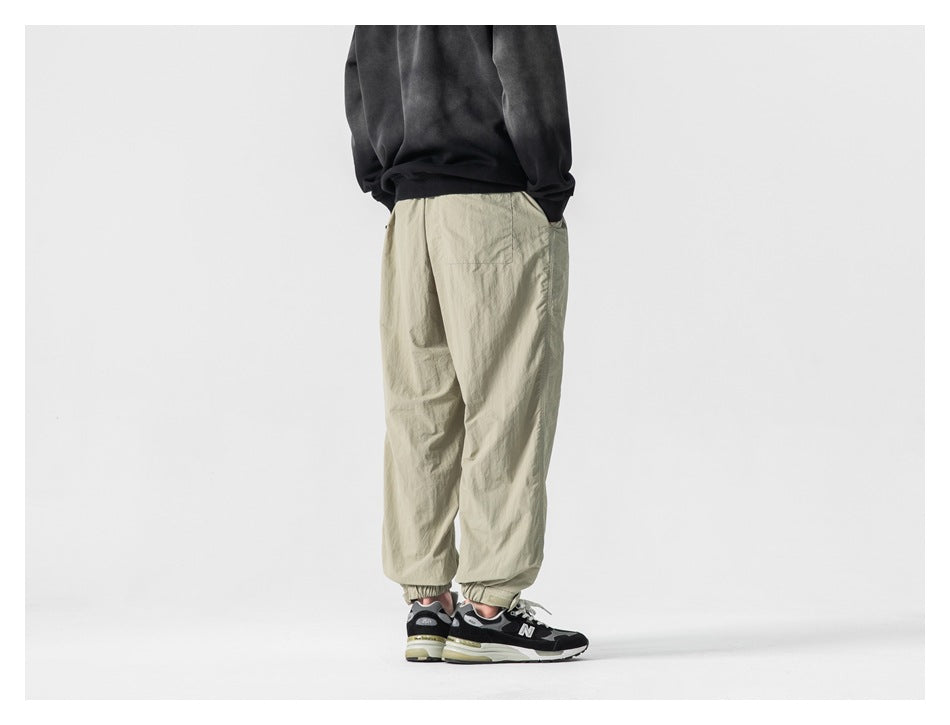 Rear view of a model wearing light khaki jogger pants with elastic ankle cuffs.