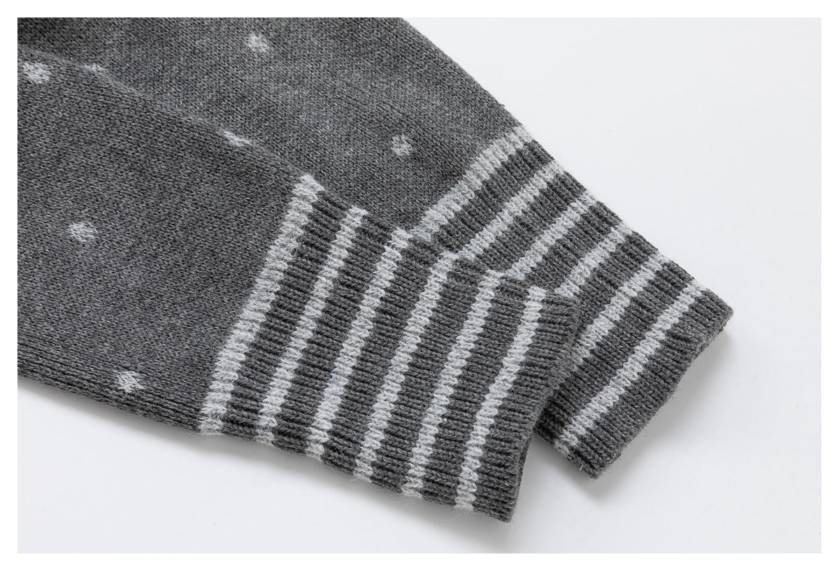 Close-up of a gray cardigan sleeve with small white dots and a wide striped ribbed cuff.