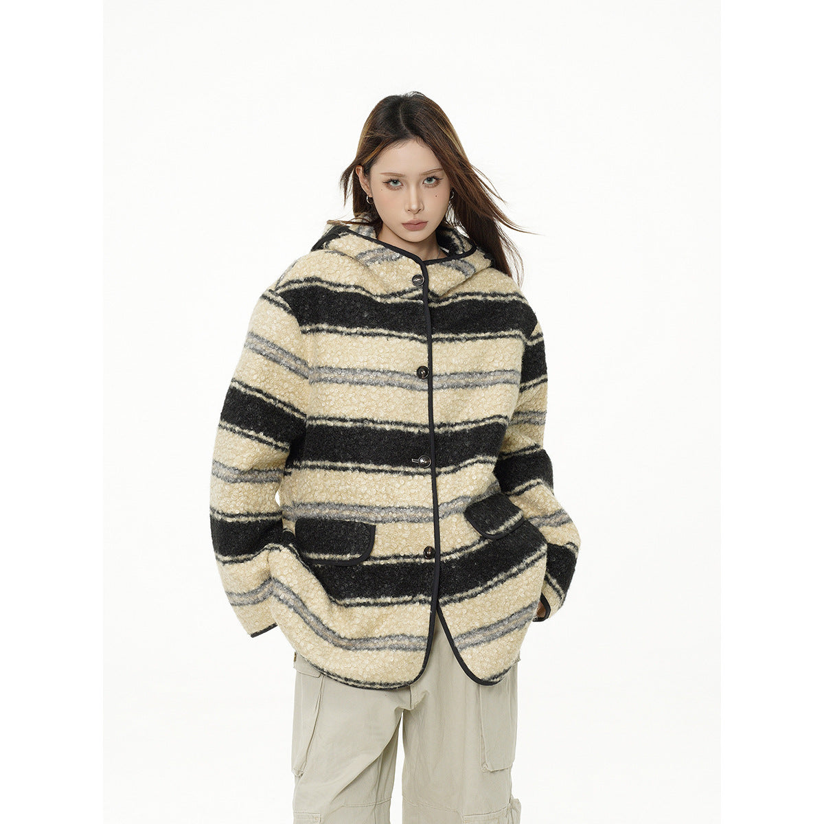 Closer front view of a model in a cream, black, and gray striped hooded jacket with dark trim and beige cargo pants.