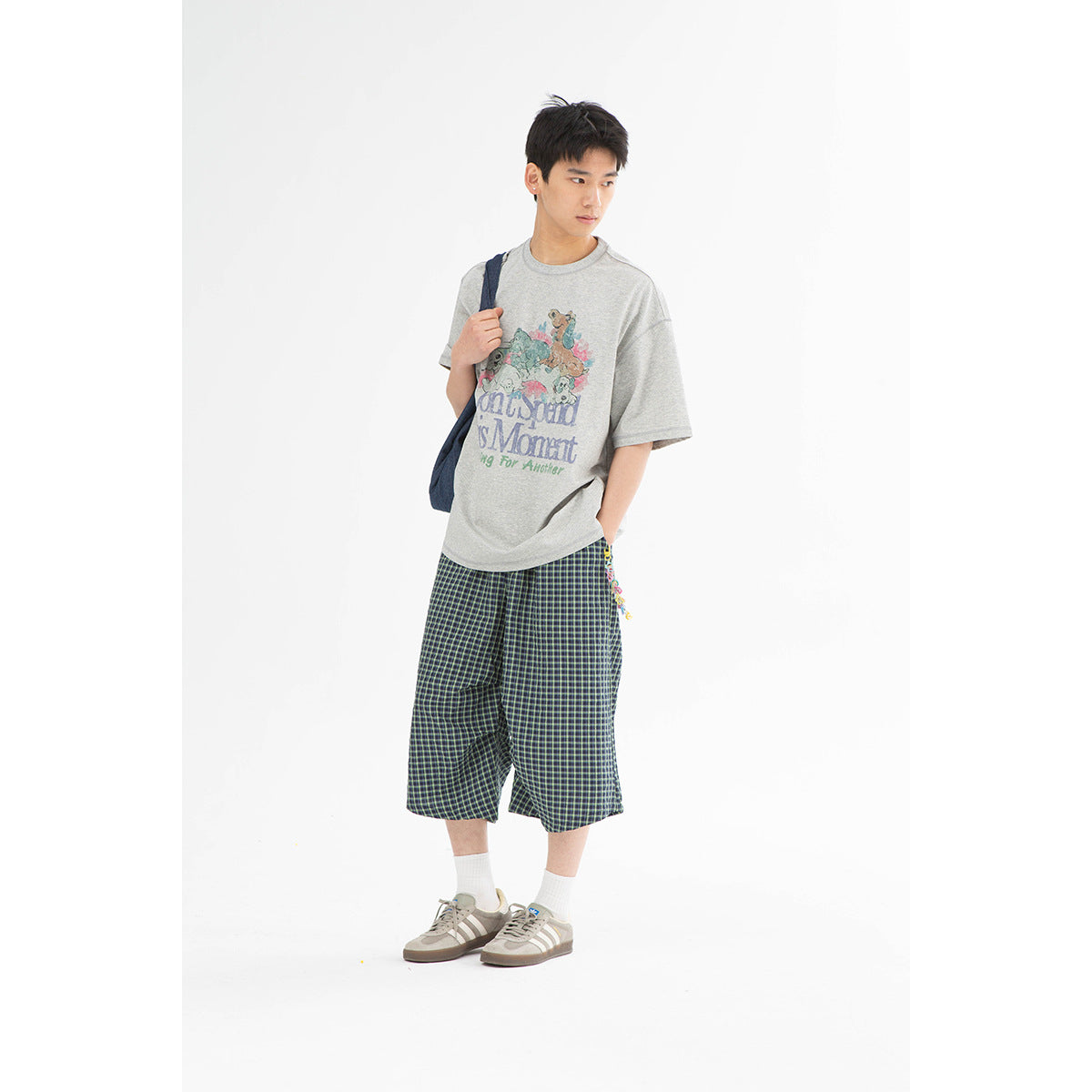 Model wearing a gray graphic T-shirt with dark plaid knee-length shorts.