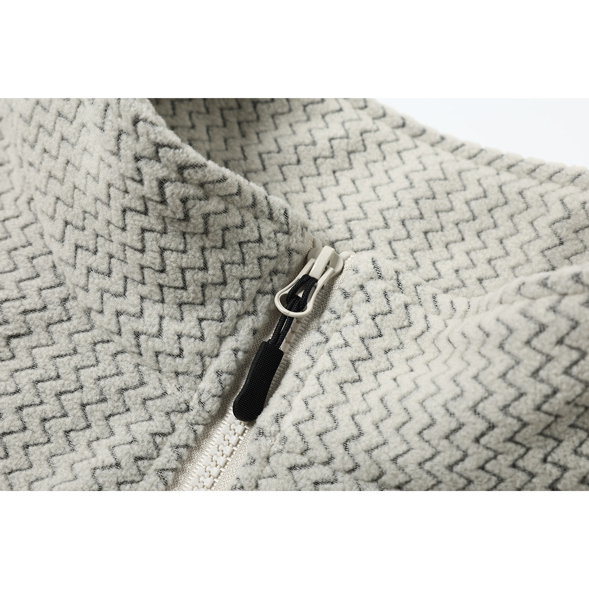 Close-up of a cream and gray zigzag-patterned garment with a white zipper and black pull.