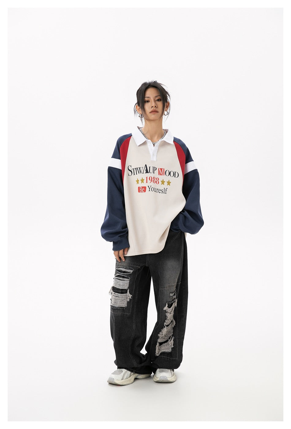 Full-length front view of a model wearing a cream polo sweatshirt with navy sleeves, red shoulder panels, and black ripped