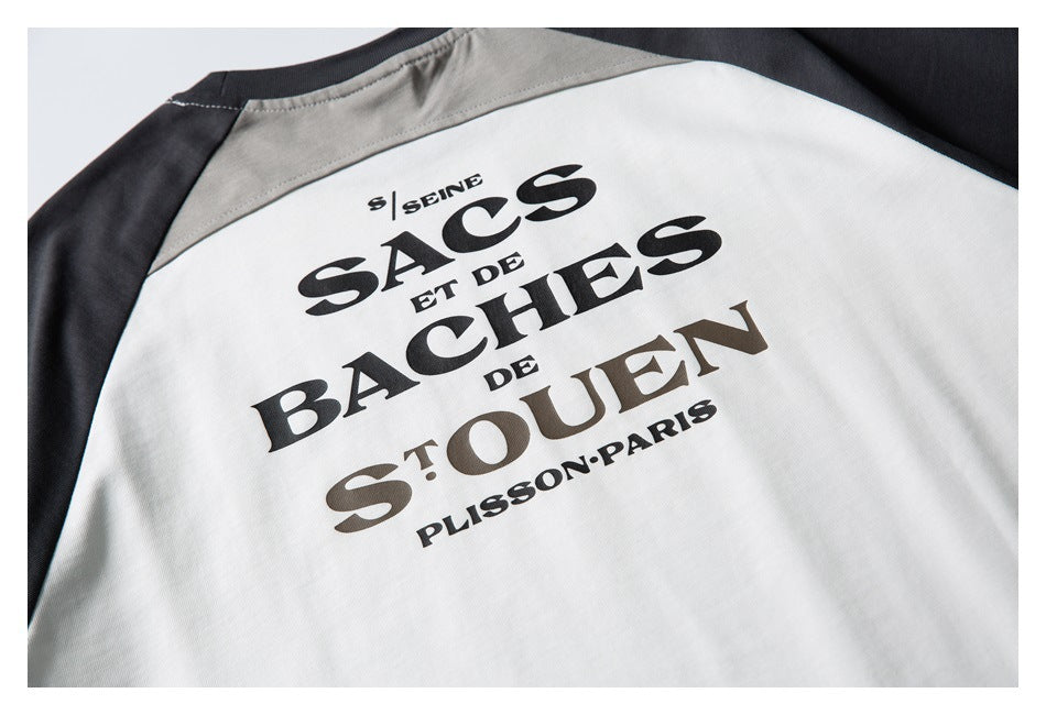 Close-up of the large black French text graphic across the back of a white raglan T-shirt with charcoal sleeves.