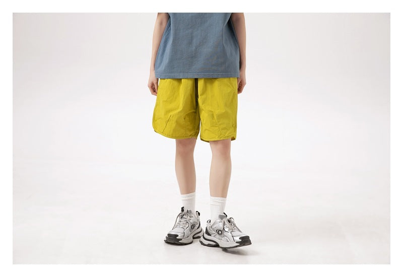 Cropped front view of a person wearing bright yellow knee-length shorts with a blue-gray sleeveless top.