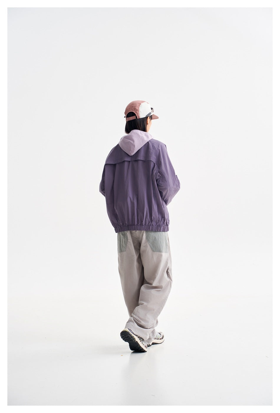 Rear view of a model wearing a purple hooded jacket with an elastic hem.