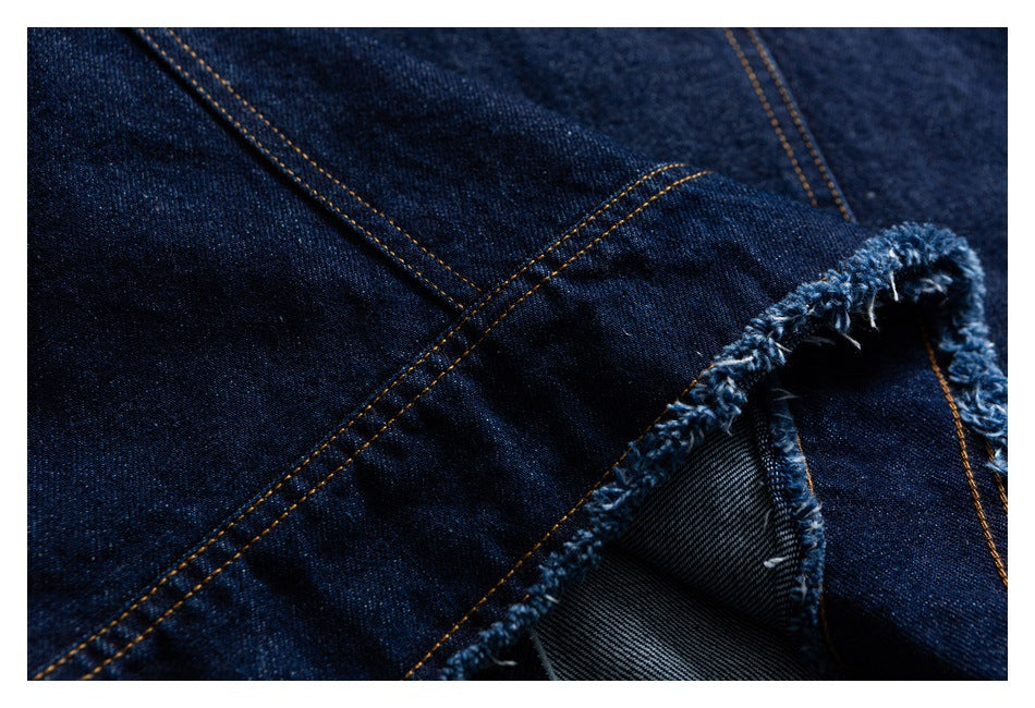 Close-up of dark indigo denim with orange topstitching and a frayed seam edge.