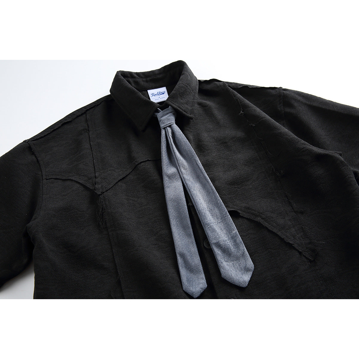 Close-up of a black collared shirt with angular seam details and a long gray tie.