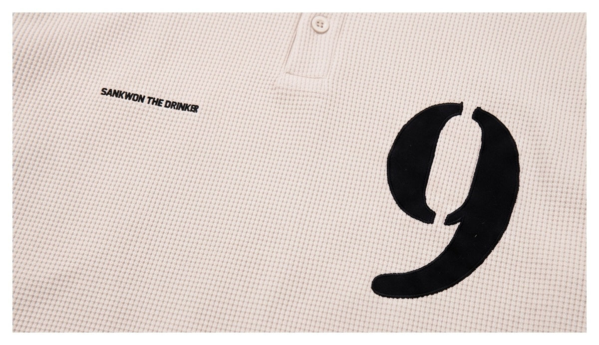 Close-up of the cream polo's chest print: black text and a large black number 9.
