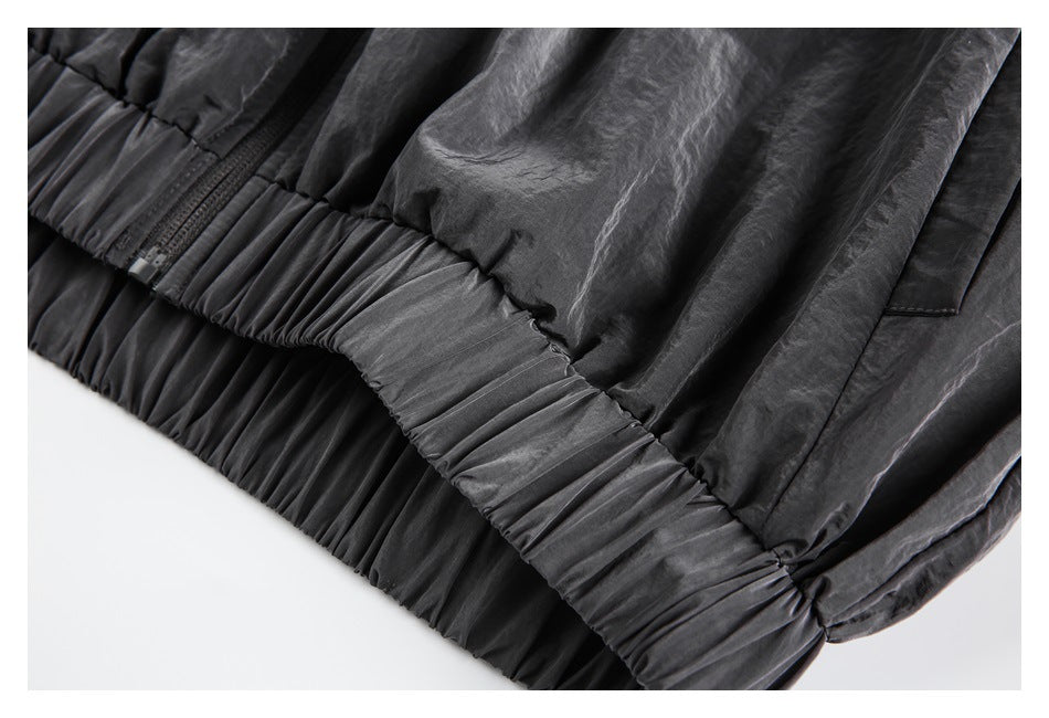 Close-up of a dark charcoal garment’s gathered elastic hem, zipper, and stitched side pocket.