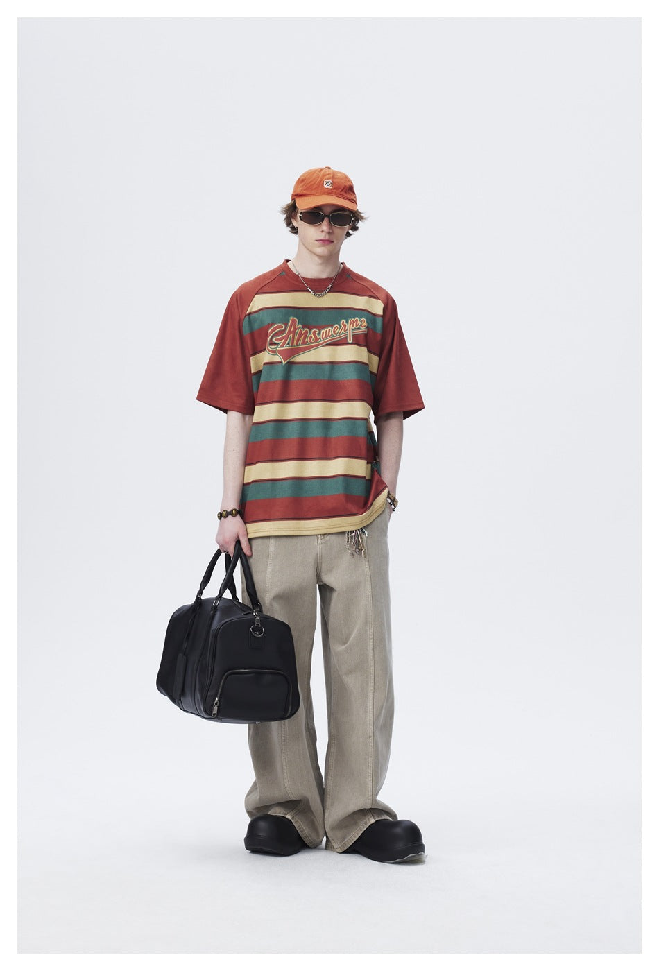 Front view of a model in a rust, teal and cream striped graphic T-shirt and loose beige trousers.