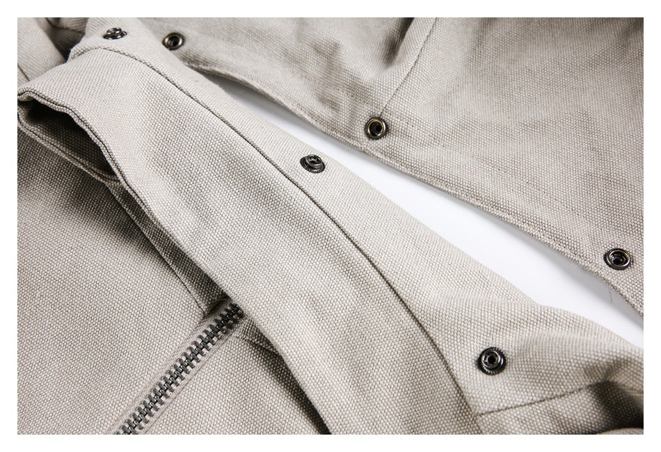 Close-up of a light taupe jacket showing textured fabric, metal snaps, and a zipper edge.