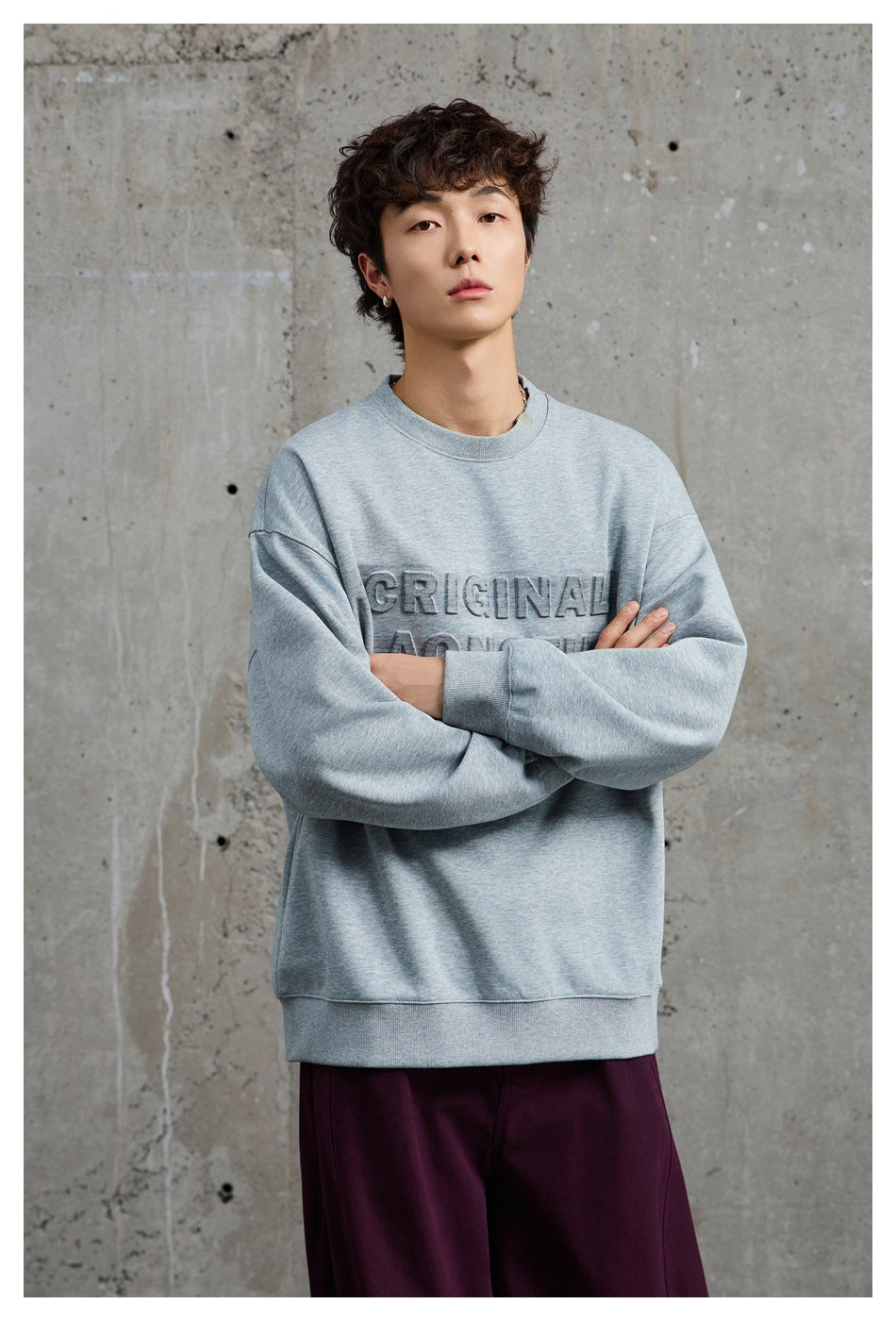 Closer view of a model wearing a light gray oversized crewneck sweatshirt with raised chest lettering.