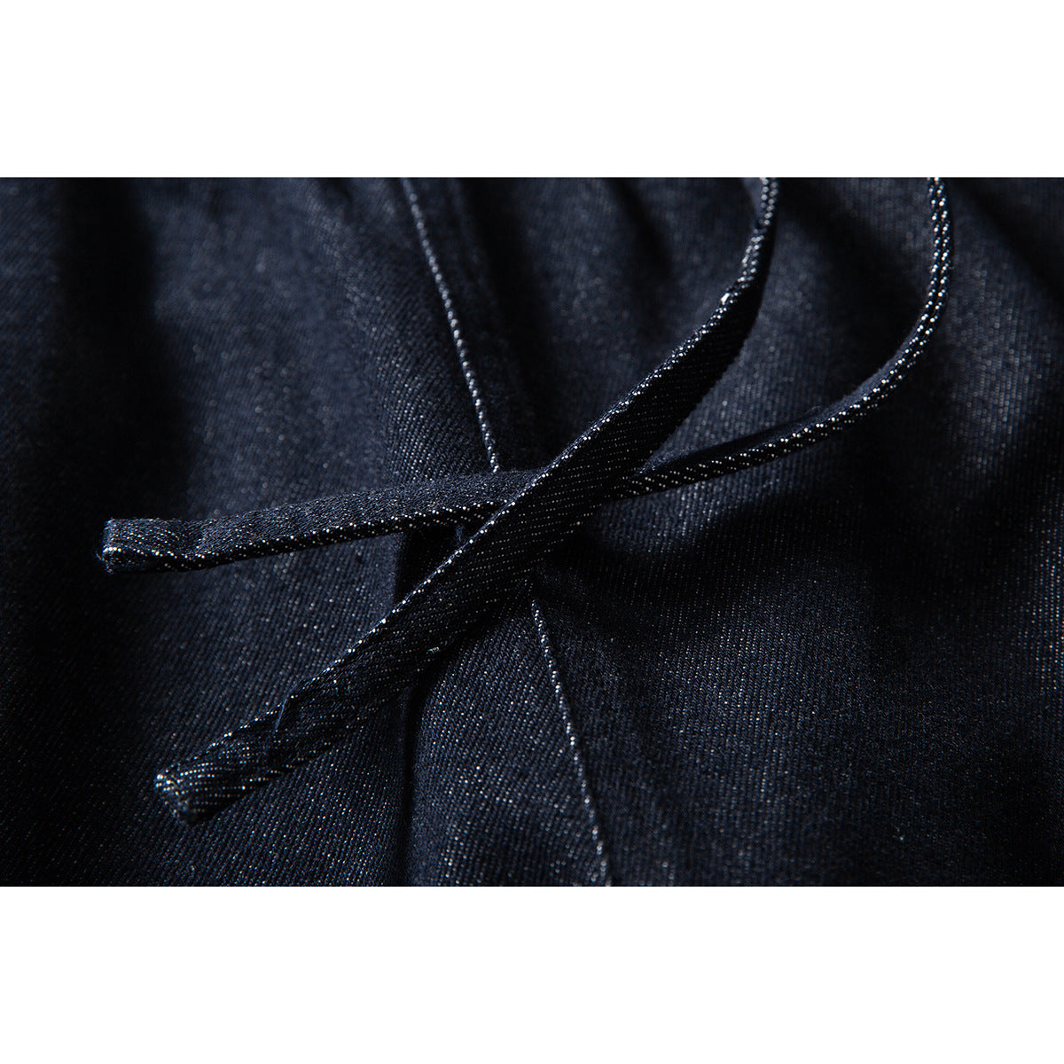 Close-up of dark indigo pants with a matching fabric drawstring tied at the waist.