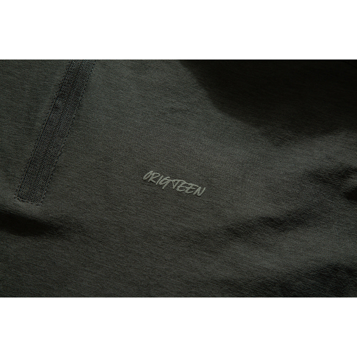 Close-up of a charcoal shirt with a small embroidered chest logo and zipper trim.