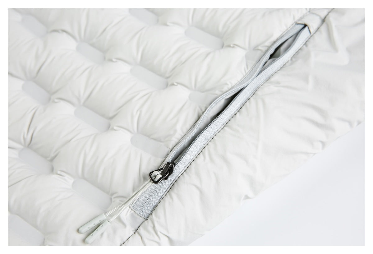 Close-up of a gray diagonal zipper partly open on the white padded jacket, with two pull cords.
