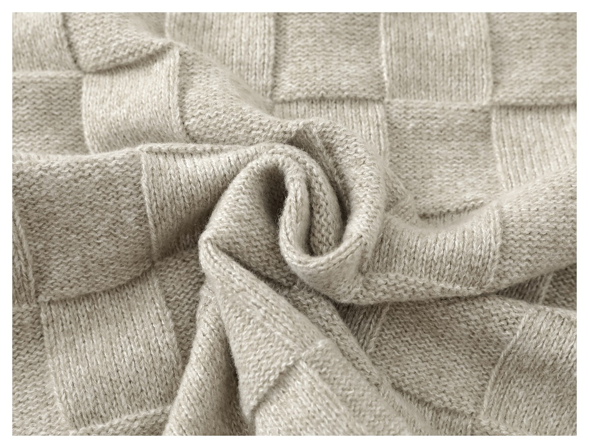 Close-up of light beige knit fabric with a raised checkerboard texture and a folded, draped section.
