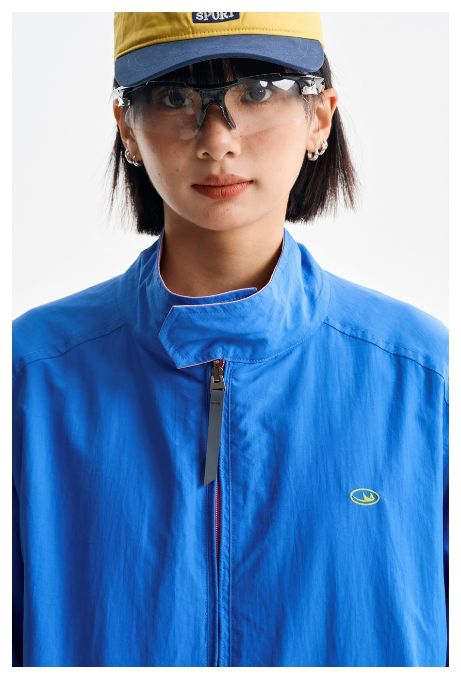 Close view of a bright blue jacket's high collar, front zipper, and small oval chest emblem.