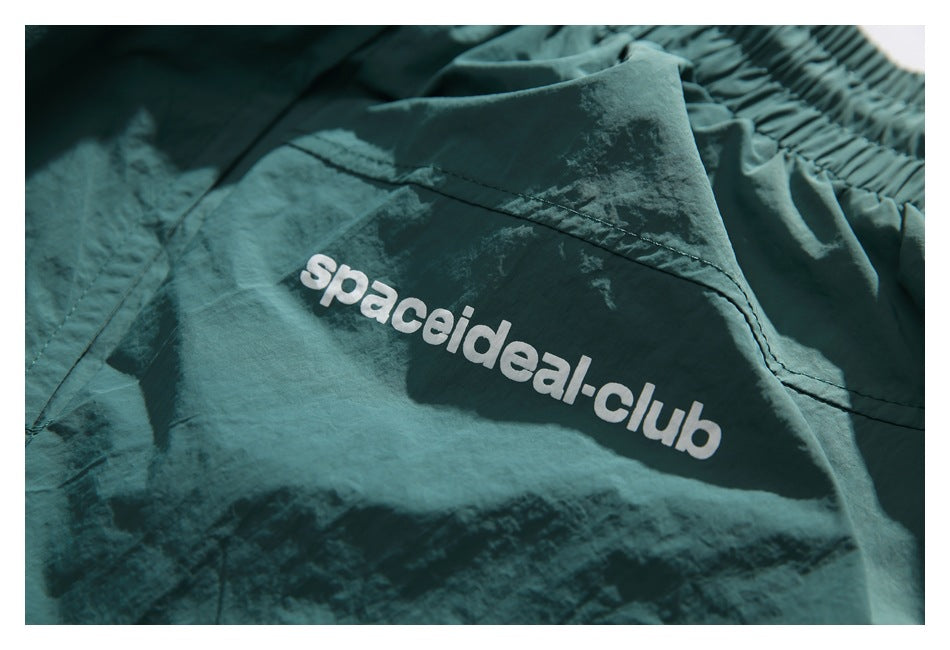Close-up of white spaceideal-club lettering printed on teal shorts.