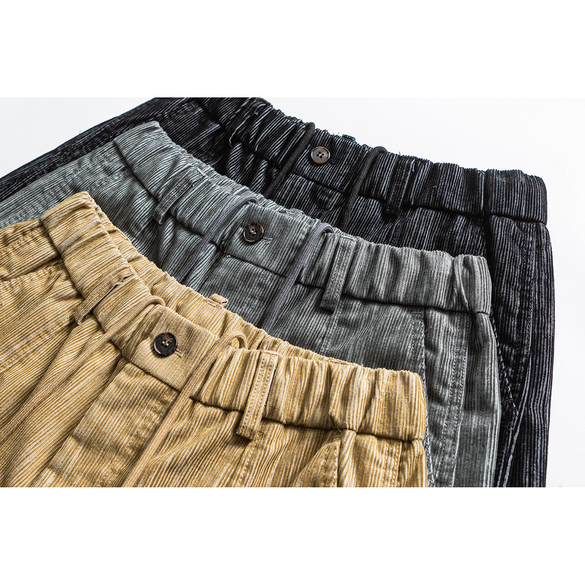 Close-up of elastic waistbands and button details on tan, gray, and black trousers.