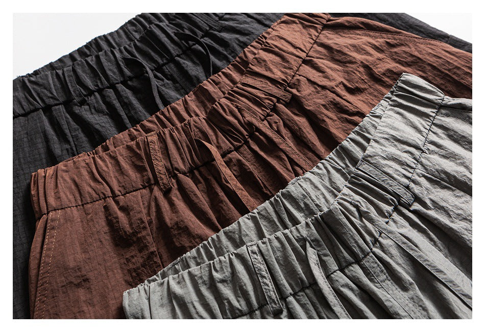 Close-up of the gathered waistbands and fabric of loose cargo pants in black, brown, and gray.