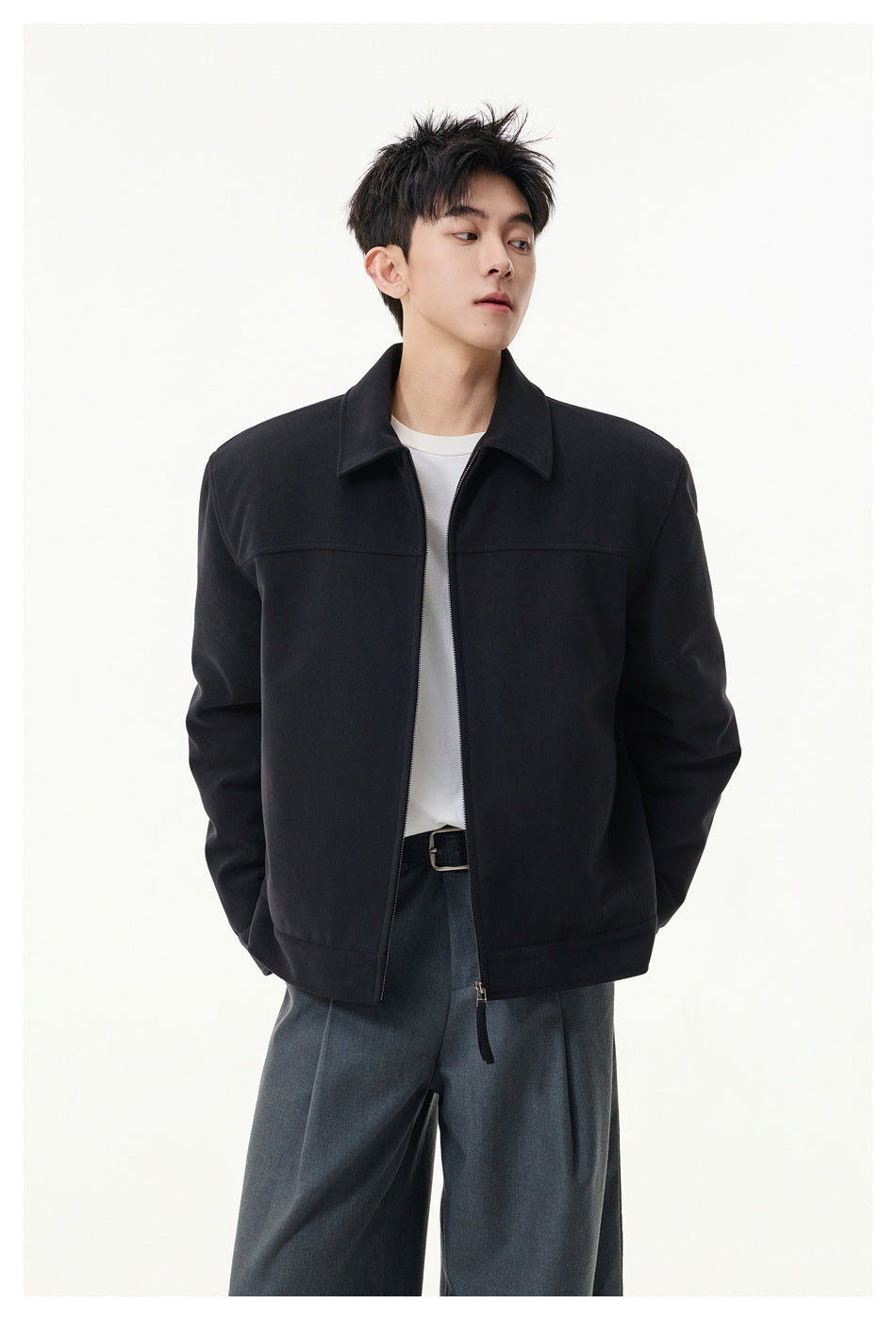 Model wearing an open black collared zip jacket over a white tee and gray pleated trousers, front view