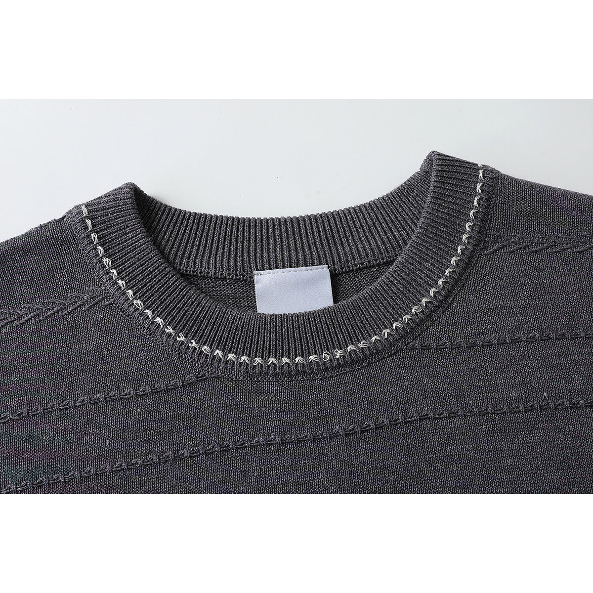 Close-up of a charcoal knit top's ribbed crew neck and decorative light-colored stitching.
