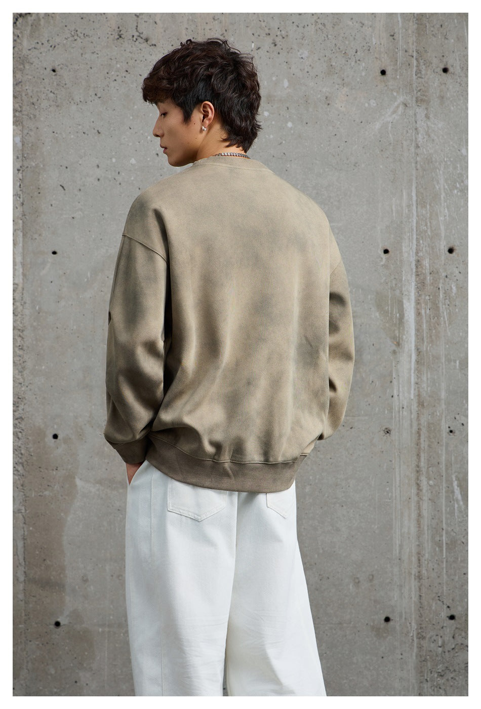 Model wearing a loose taupe crewneck sweatshirt, shown from the back with white wide-leg trousers.