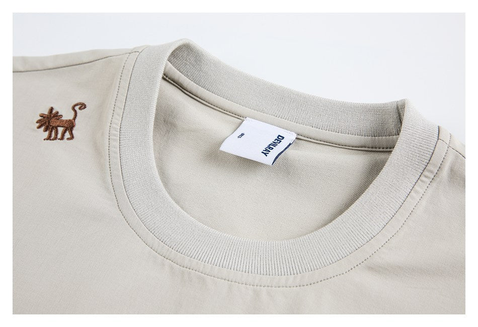 Close-up of a beige crew neckline, ribbed collar, sewn-in label, and small brown embroidered animal.