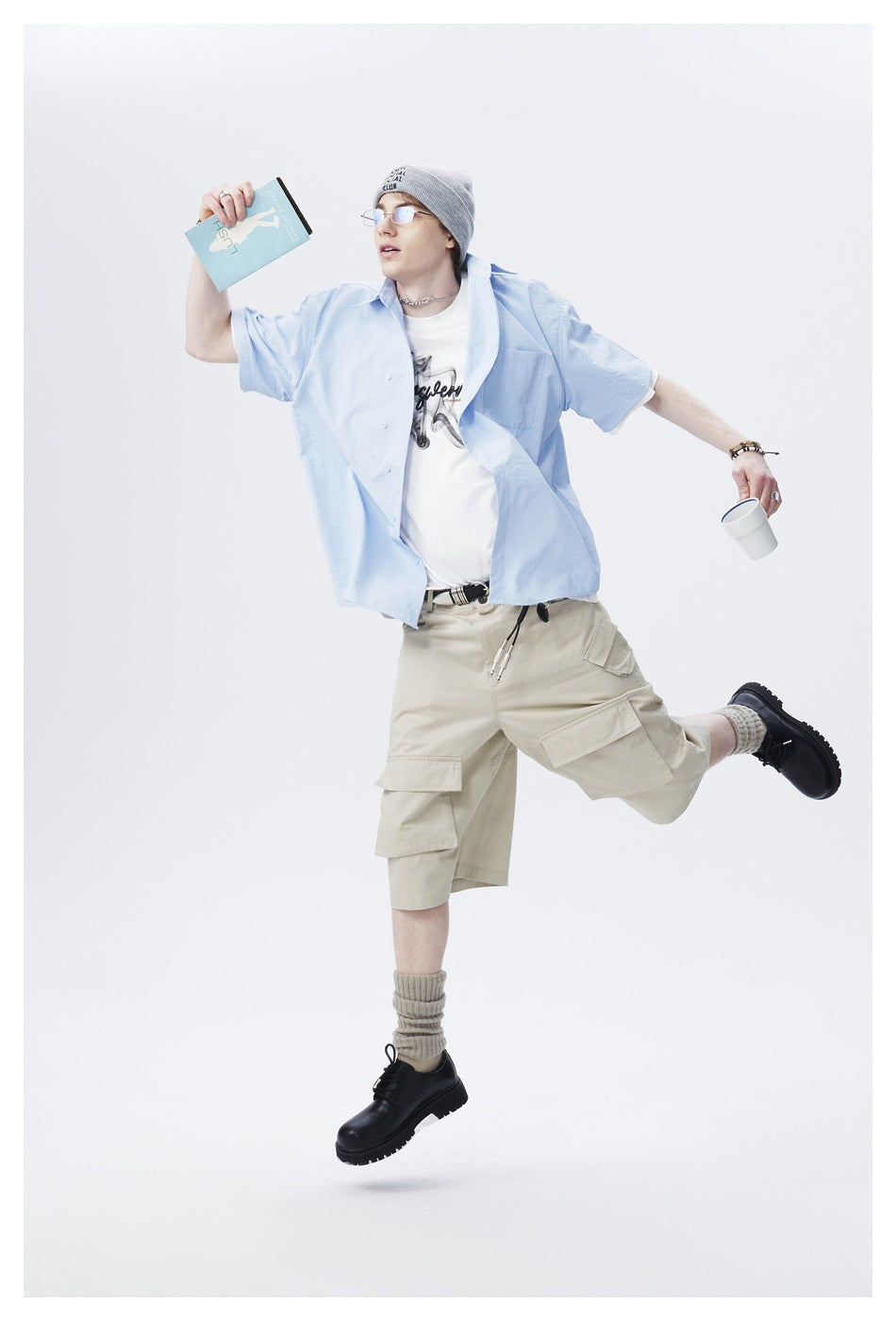 Model in a light blue short-sleeve shirt and beige cargo shorts, posing with arms outstretched.